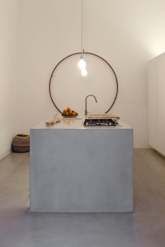 Kitchen island beneath a circular wall sculpture and pendant lights, La Corte, Nardò