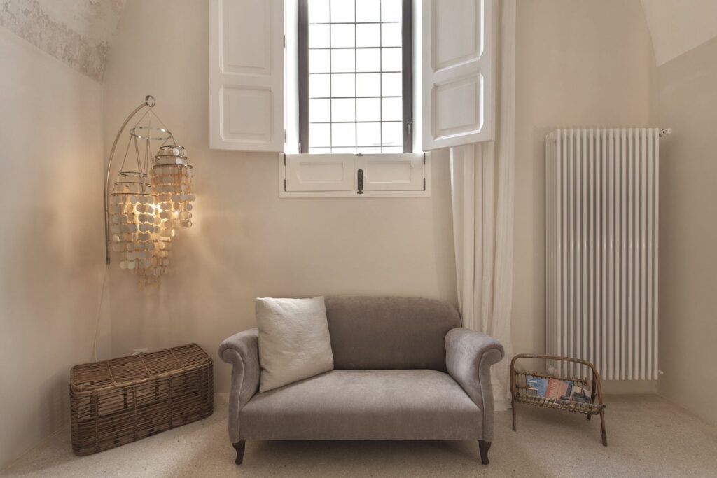 Bedroom sitting nook with a sculptural wall lamp and loveseat, Teatro house, Nardò