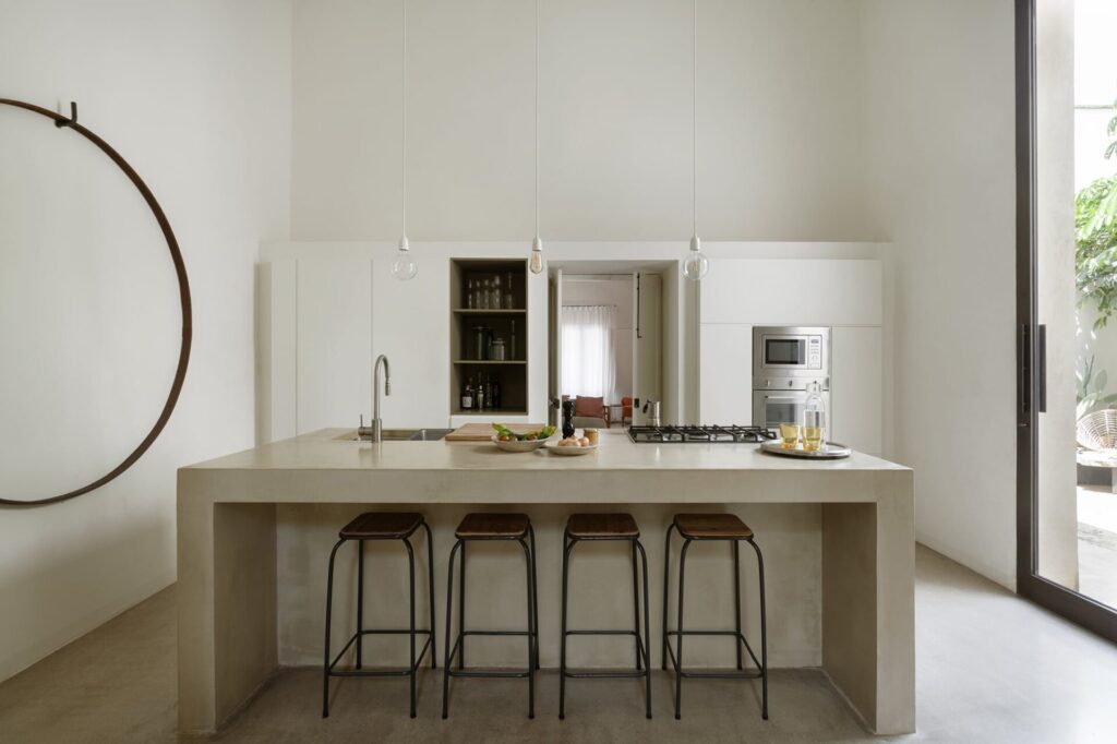 14. La_Corte_Nardòsalento_Credits40Mirrors_kitchen_003_Kitchen Concrete kitchen island with barstools and a circular wall sculpture, La Casa Grande, Nardò