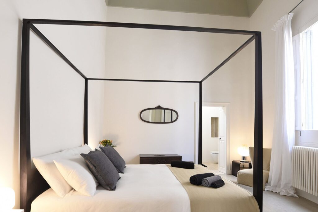 Master bedroom with dark four-poster bed frame, La Corte palazzo, Nardò