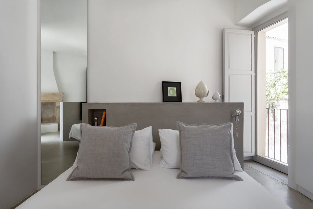 Bedroom 2 with grey linen pillows and a fireplace reflected in the mirror, Agrumeto house, Nardò