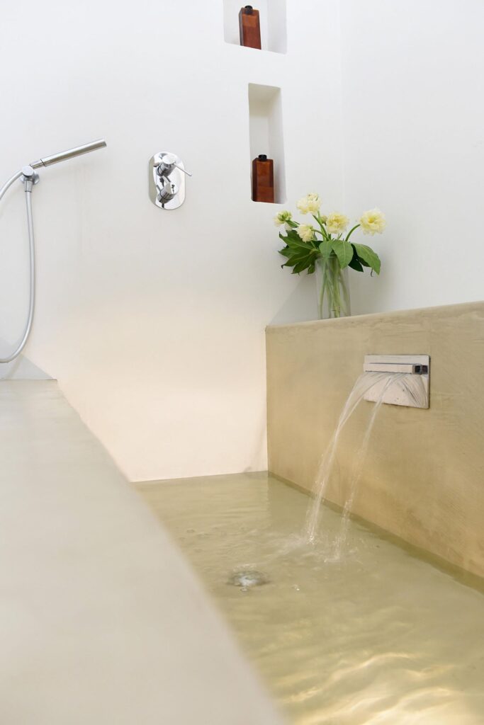Sunken tub filling with water beside a vase of flowers, La Corte master bathroom, Nardò
