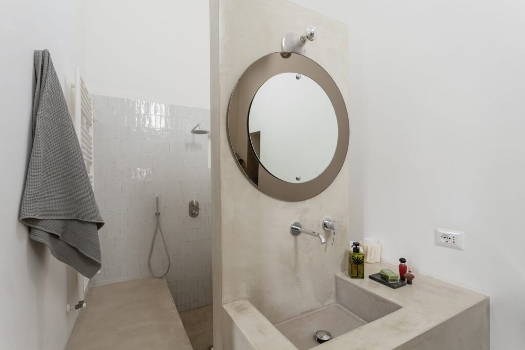 22. La_Corte_Nardòsalento_Credits40Mirrors_Bagno_007_Ensuite bathroom master bedroom Ensuite bathroom with a round mirror and microcement sink, La Casa Grande, Nardò