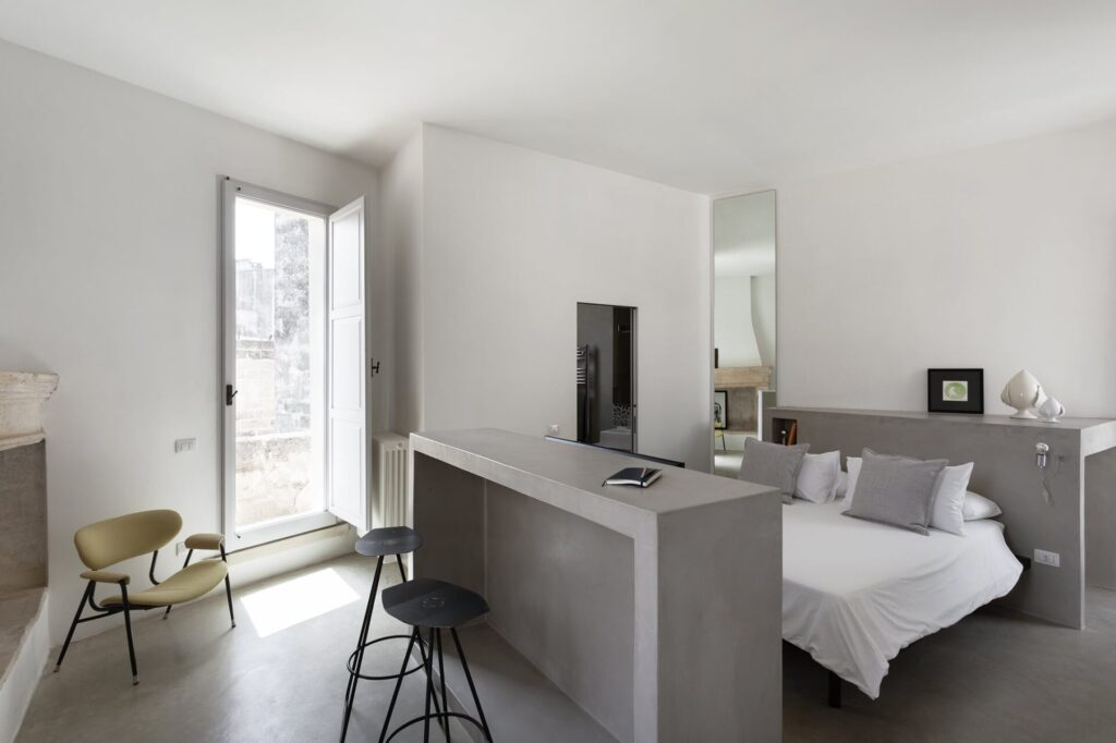 23. Agrumeto_Nardòsalento_Credits40Mirrors_022_bedroom2 Bedroom with grey linen pillows and a fireplace reflected in the mirror, La Casa Grande, Nardò