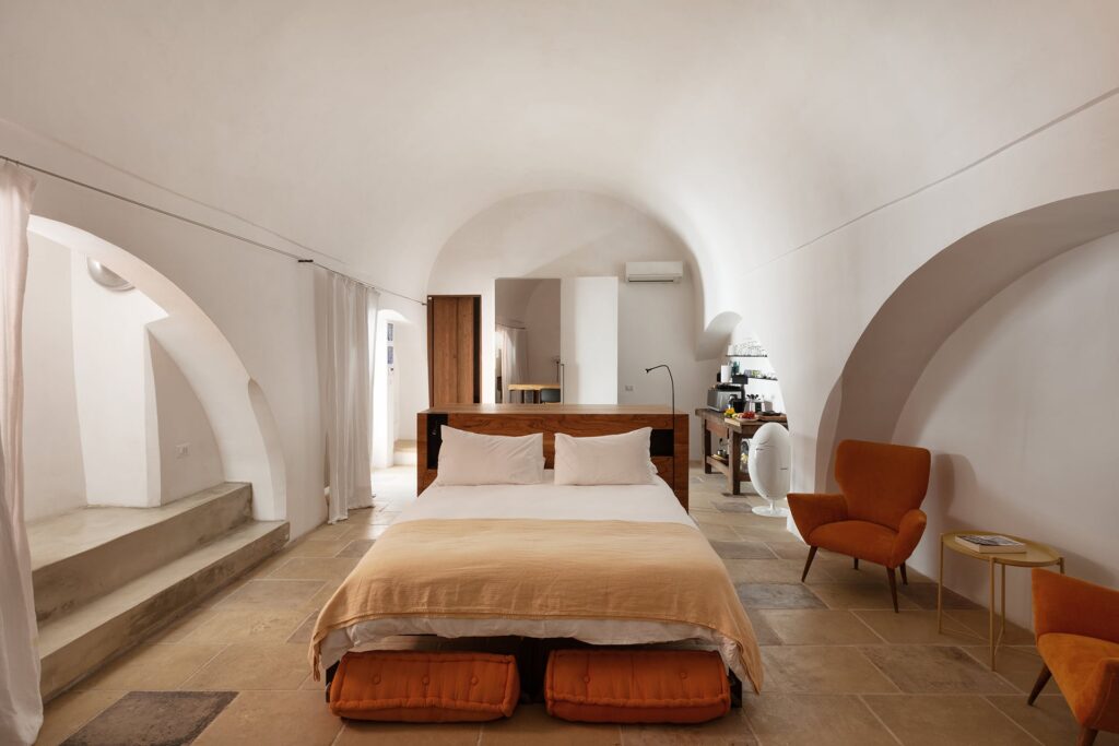 Vaulted bedroom with rust-orange armchairs beneath stone archways, La Botte, Nardò