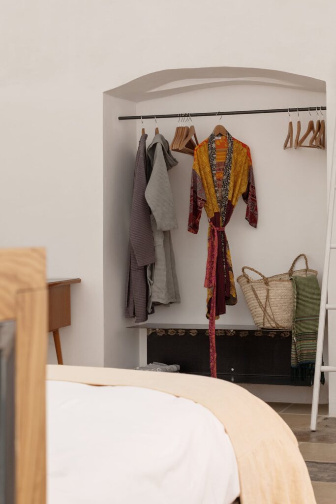 Open wardrobe nook with robes hanging beside the bed, La Botte, Nardò